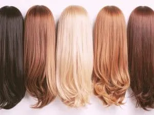 Different hair color levels displayed side by side on wigs, including black, brunette, blonde, copper, and auburn hair shades.